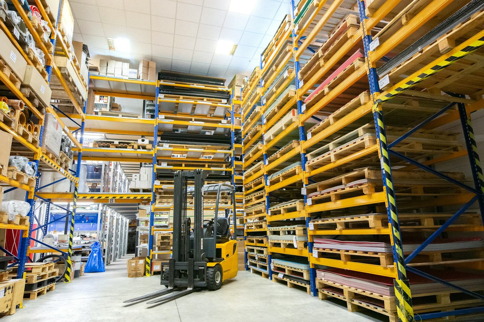 Yellow counterbalance forklift parked in a warehouse aisle between tall pallet racking