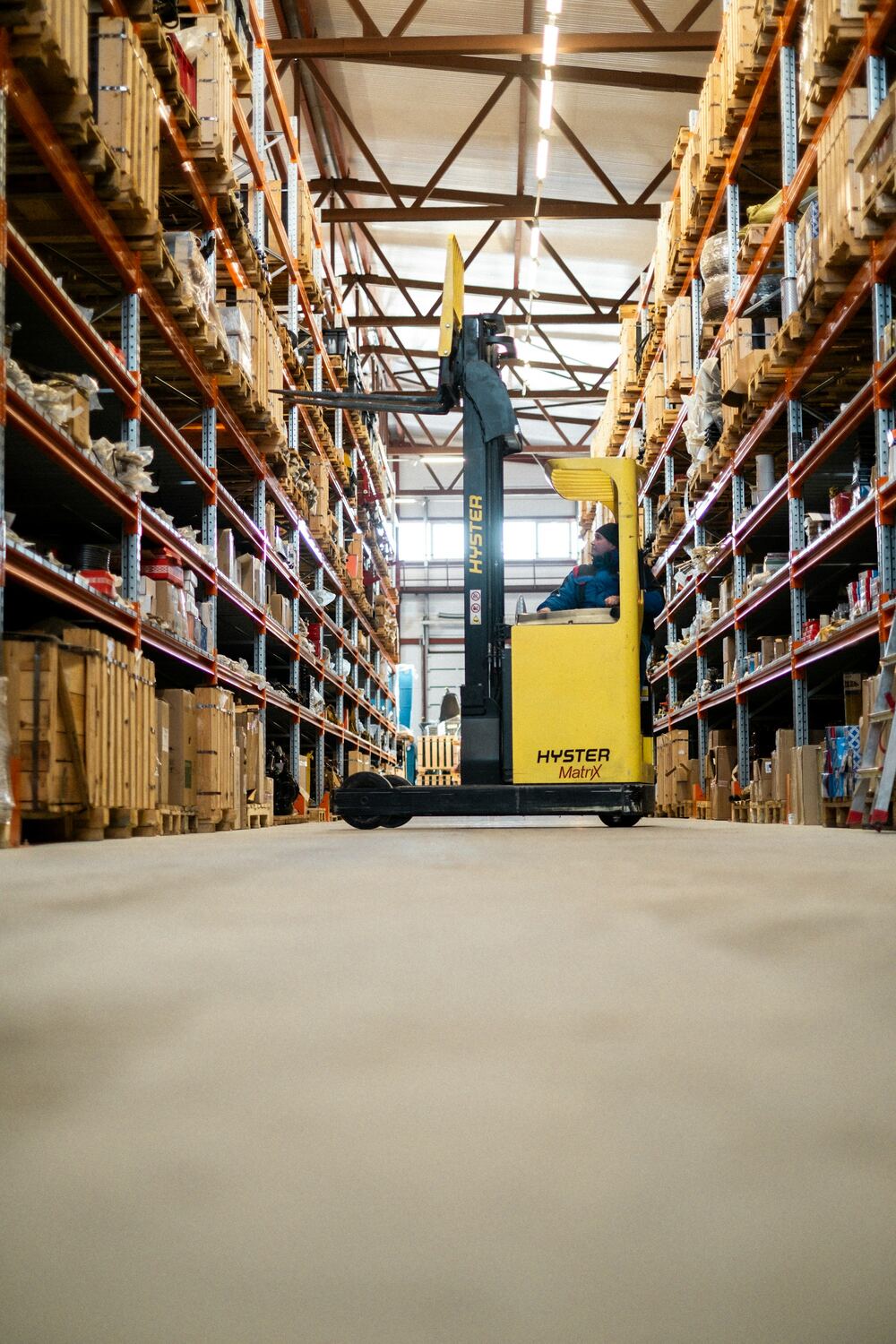 Yellow reach truck parked in a long warehouse aisle lined with pallet racking